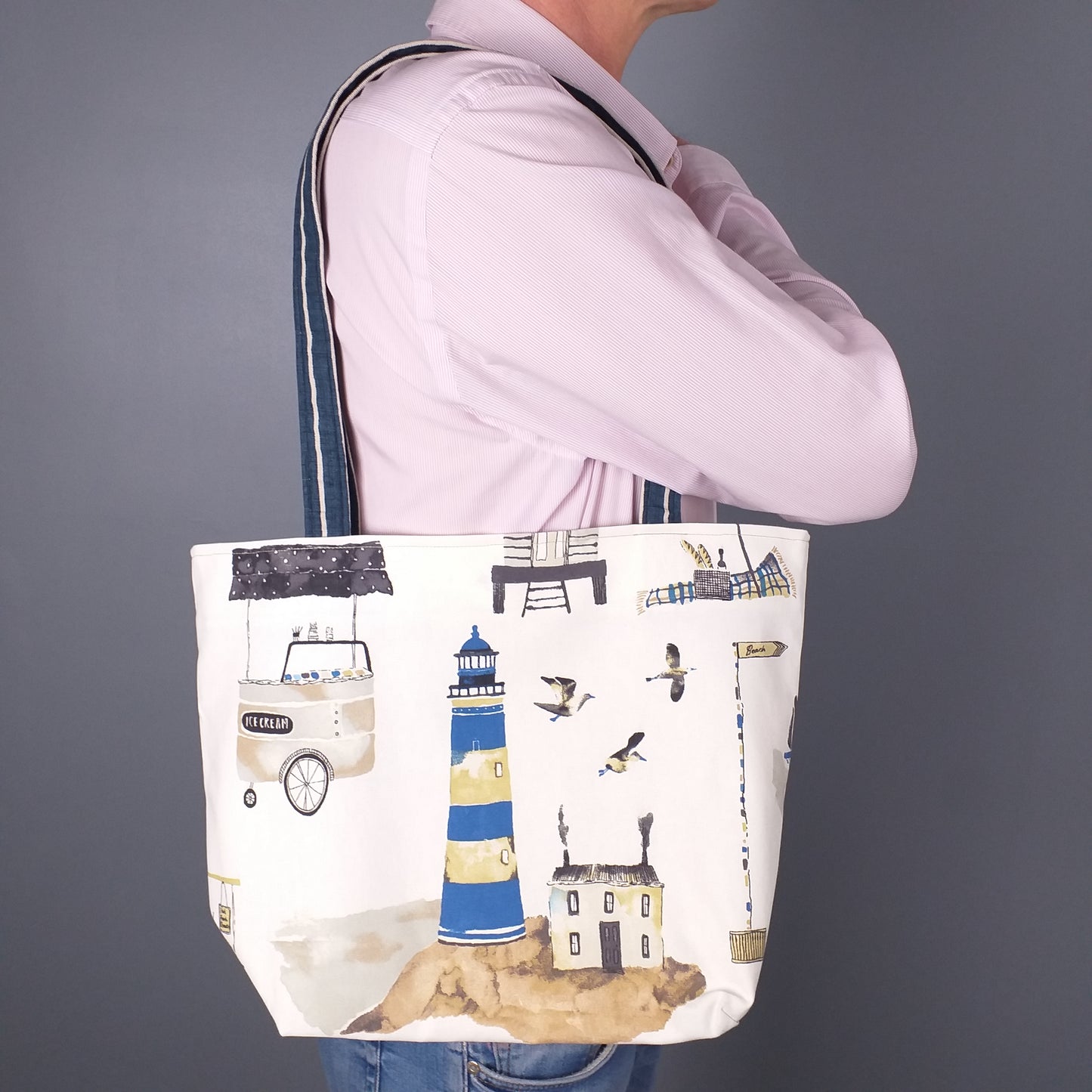 Large tote bag with multi-colour beach huts, lighthouse, seaside shops design on off-white background