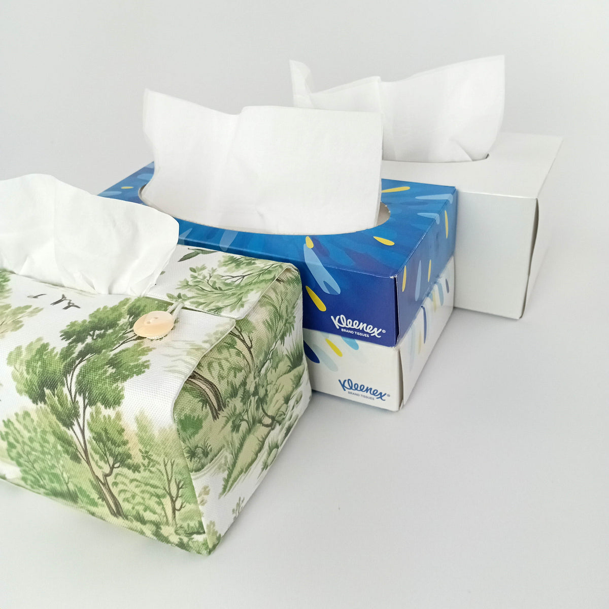 A handmade rectangular cotton tissue box cover with a green-and-white toile-style patterned shown with tissue box size options.