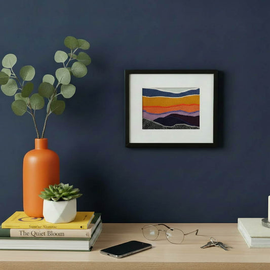 Framed fabric artwork hanging on a blue wall with a contemporary console table, vase, and mobile phone in a modern home