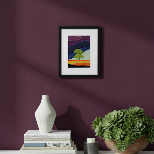 Framed fabric artwork hanging on a purple wall with a modern console table, vase, and plant