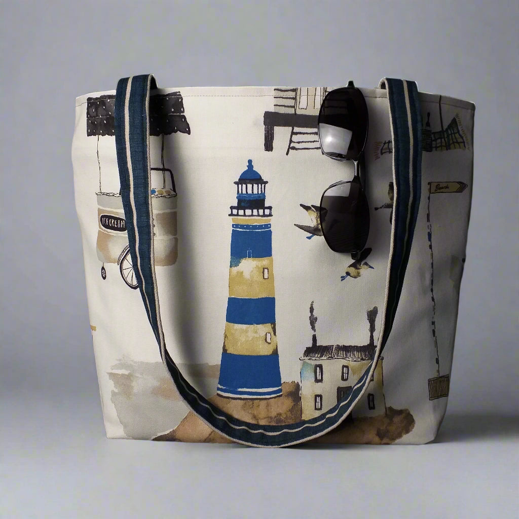 Large tote bag with multi-colour beach huts, lighthouse, seaside shops design on off-white background