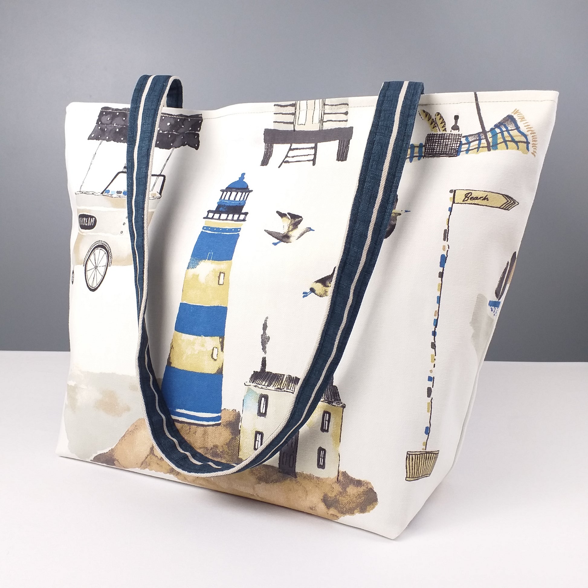 Large tote bag with multi-colour beach huts, lighthouse, seaside shops design on off-white background