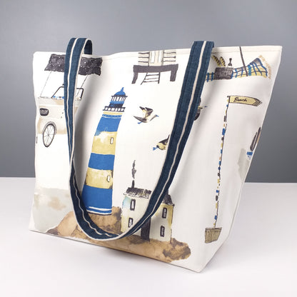 Large tote bag with multi-colour beach huts, lighthouse, seaside shops design on off-white background