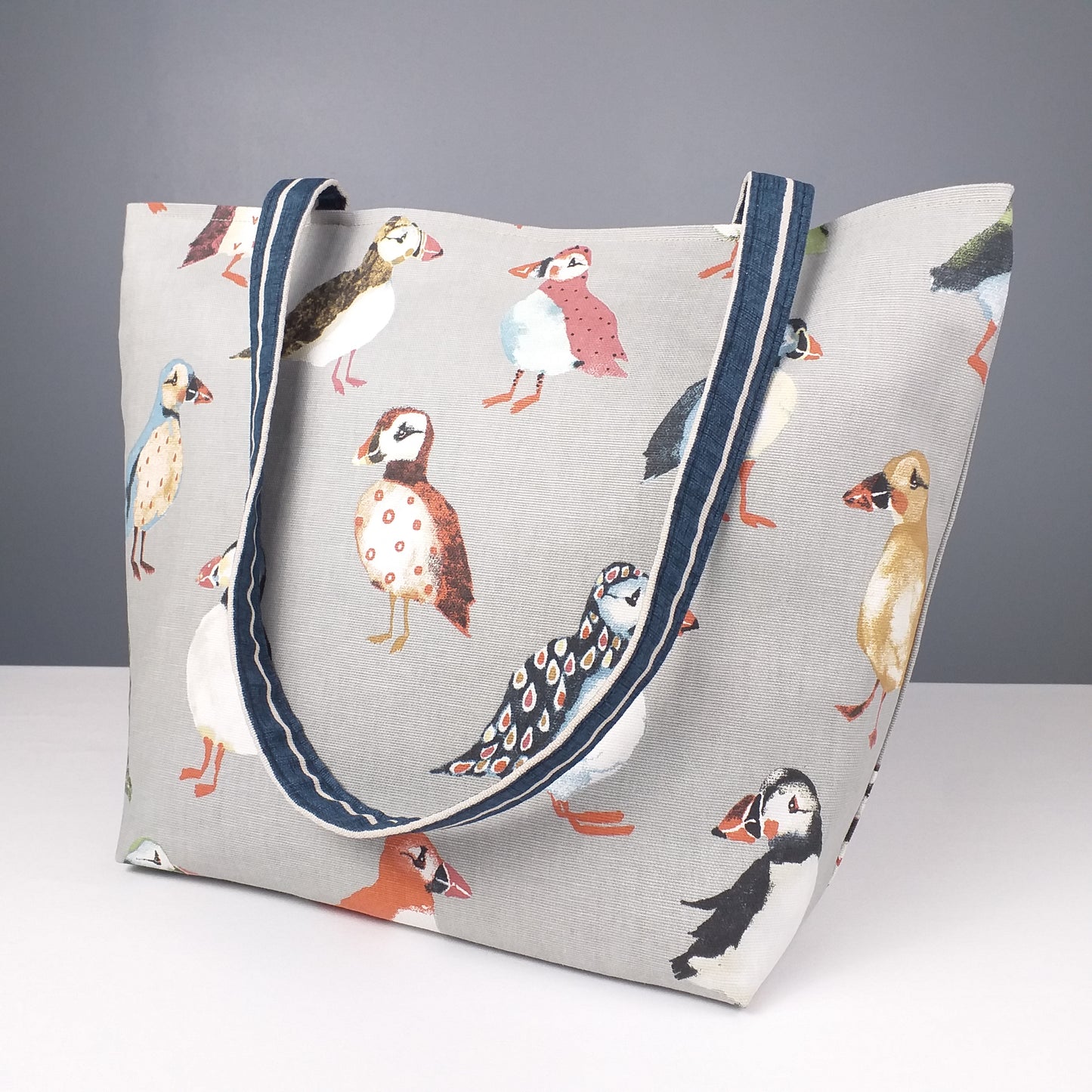 Side view of a large tote bag with multi-colour puffins design on grey background