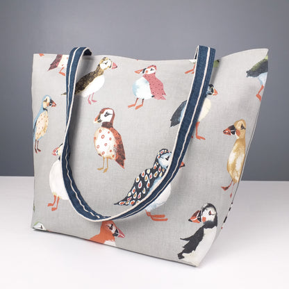Side view of a large tote bag with multi-colour puffins design on grey background