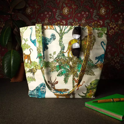 Large cotton tote bag with elephant, giraffe, water buffalo, monkey, panther, gorilla, lemur, rhinoceros design sitting on a table with a notebook, pen, and plant