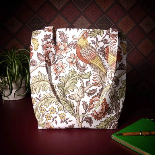Large tote bag with pheasants and flowers design on natural colour background sitting on a table with a notebook, pen, and plant