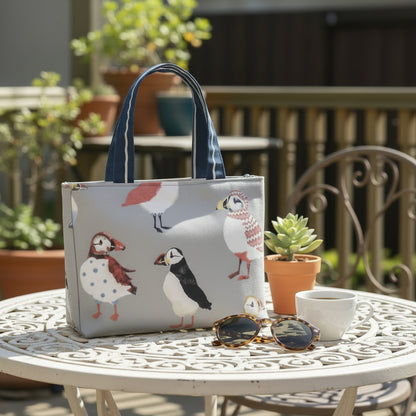 Mini tote bag with multi-colour puffins design on grey background sitting on a garden table on a patio