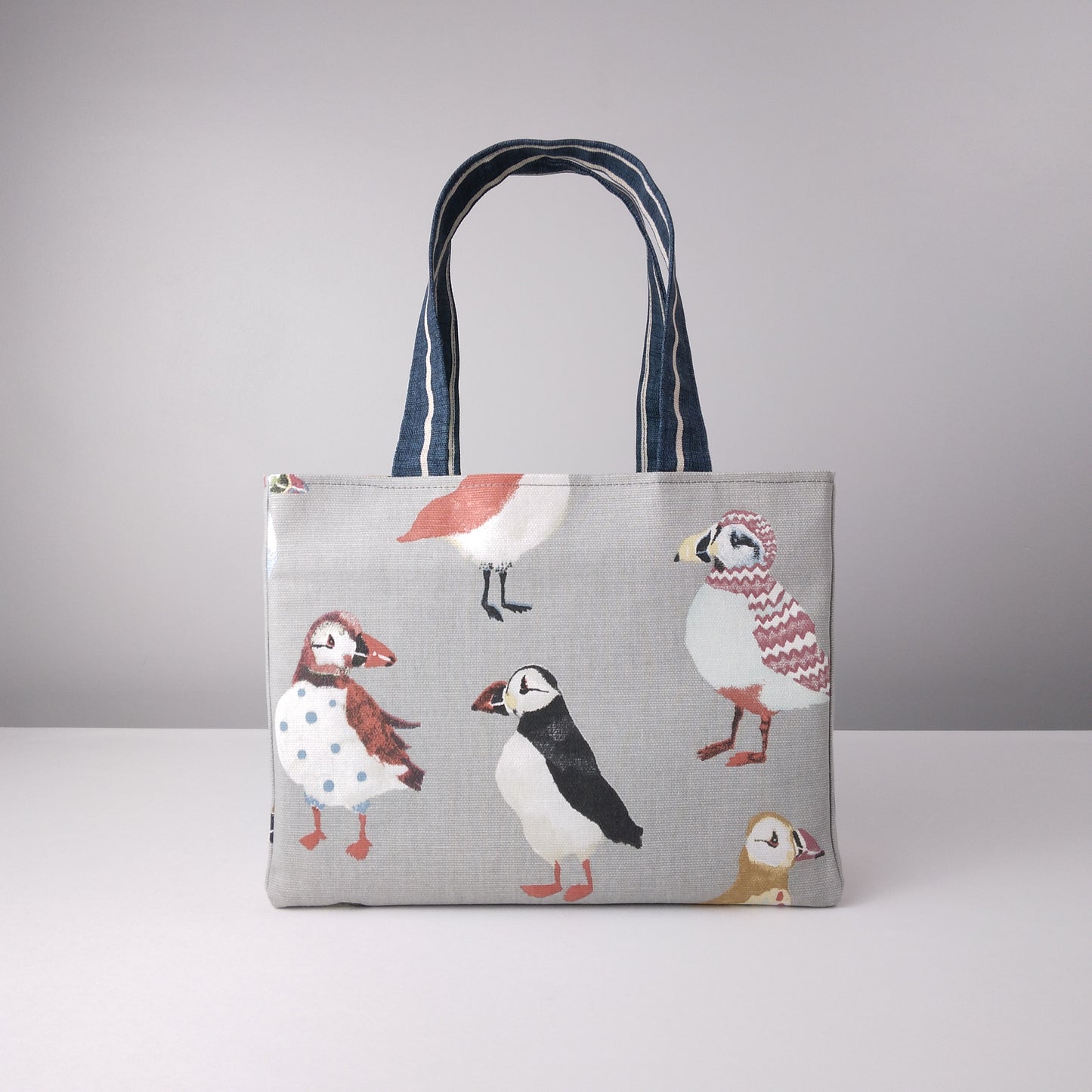 Front view of a mini tote bag with multi-colour puffins design on grey background