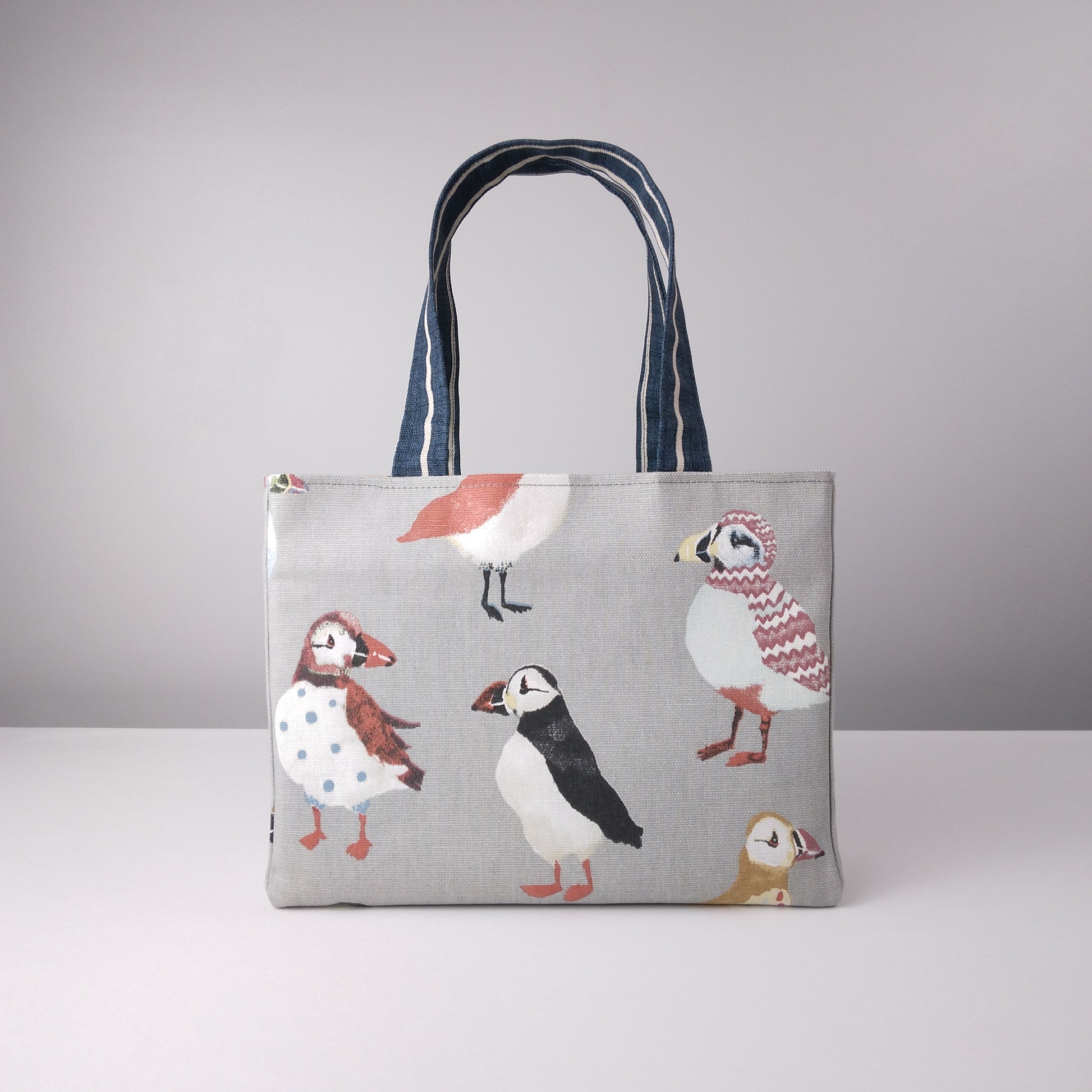 Front view of a mini tote bag with multi-colour puffins design on grey background