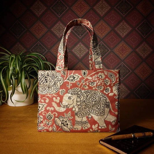Mini tote bag with ornate taupe elephant design on red background sitting on a table with notepad, pen and plant