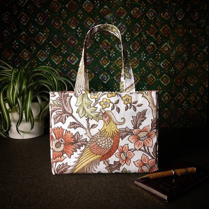 Mini tote bag with pheasants and flowers design on off-white colour background sitting on a table with notepad, pen and plant