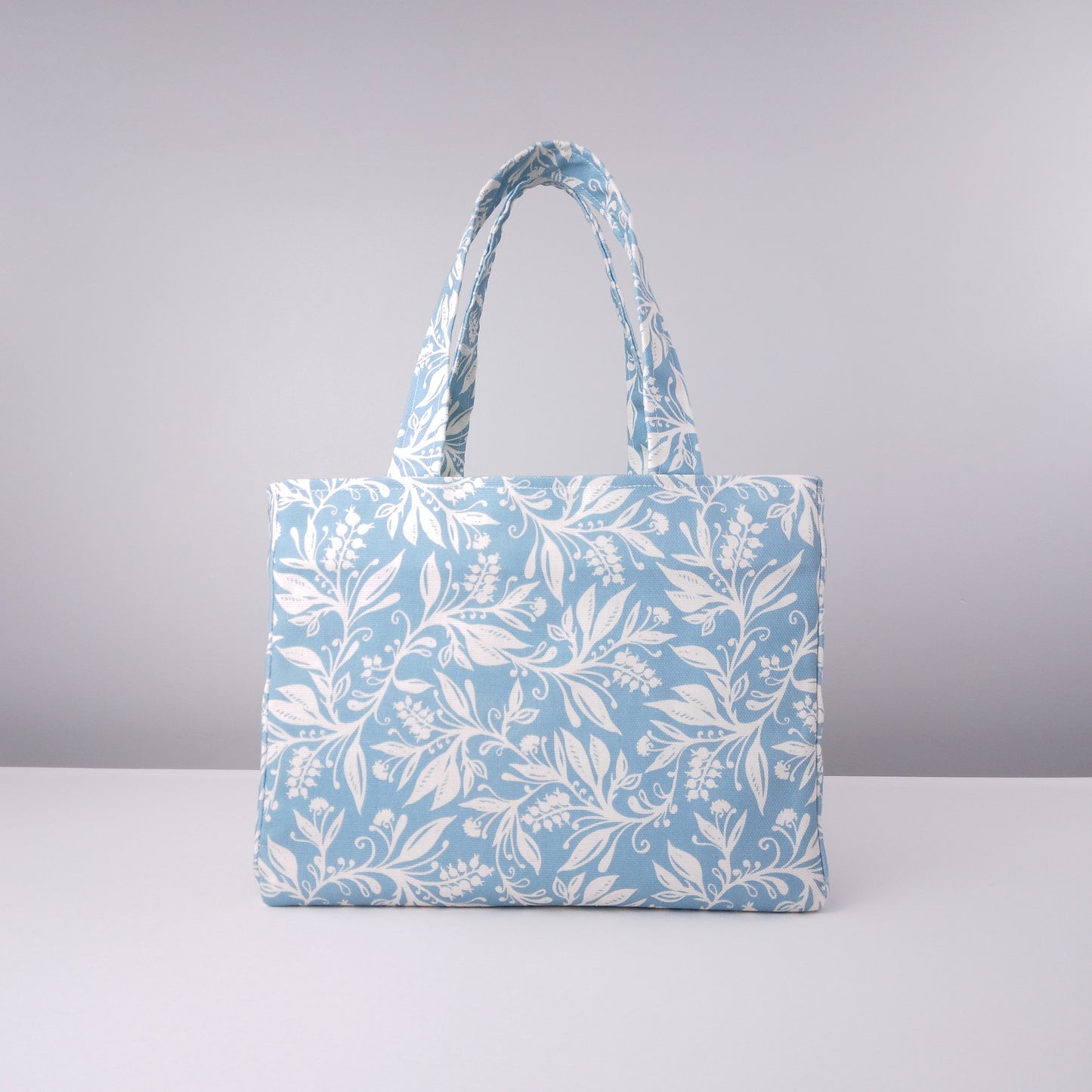 Mini tote bag with white wildflower silhouette design on light blue background