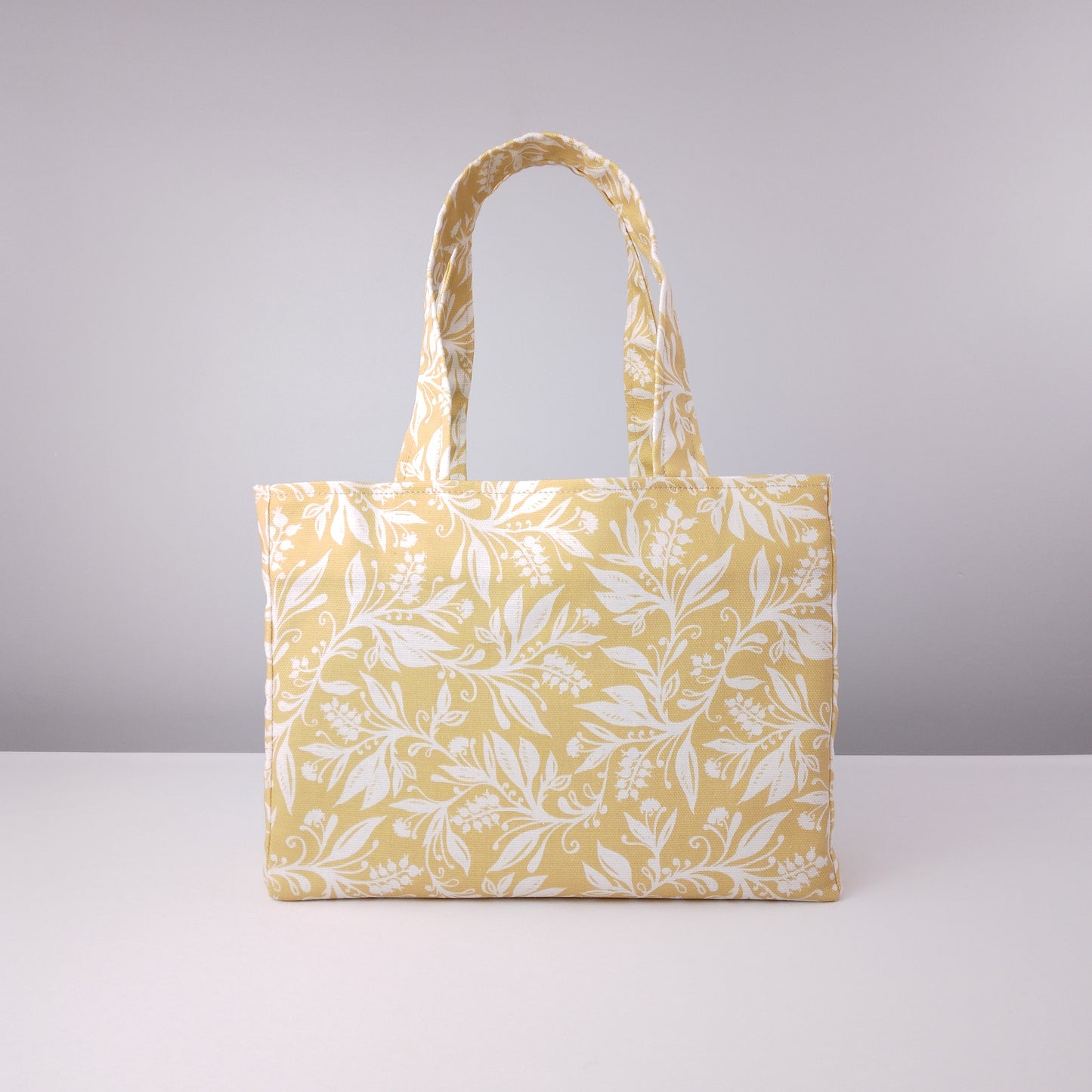 Front view of a mini tote bag with white wildflower silhouette design on yellow background