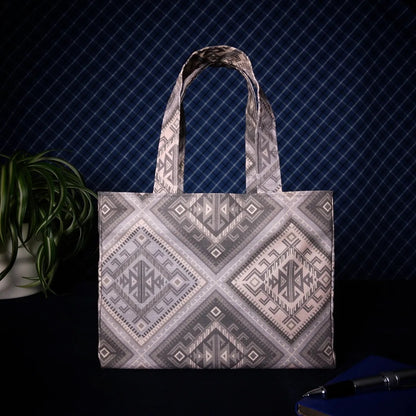 Mini tote bag with grey diamond kilim pattern sitting on a table with a notebook, pen and plant
