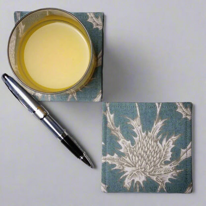 Square coasters with white thistle design on teal blue background