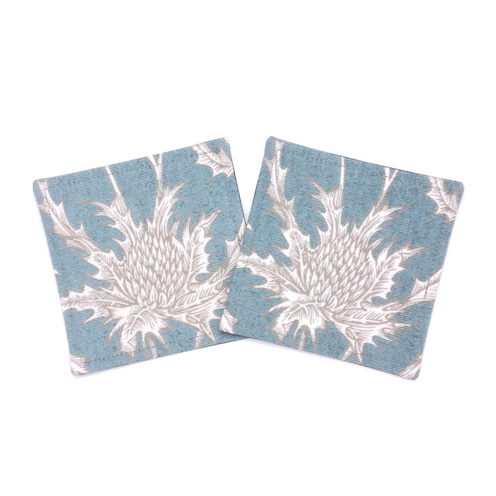 Square coasters with white thistle design on teal blue background