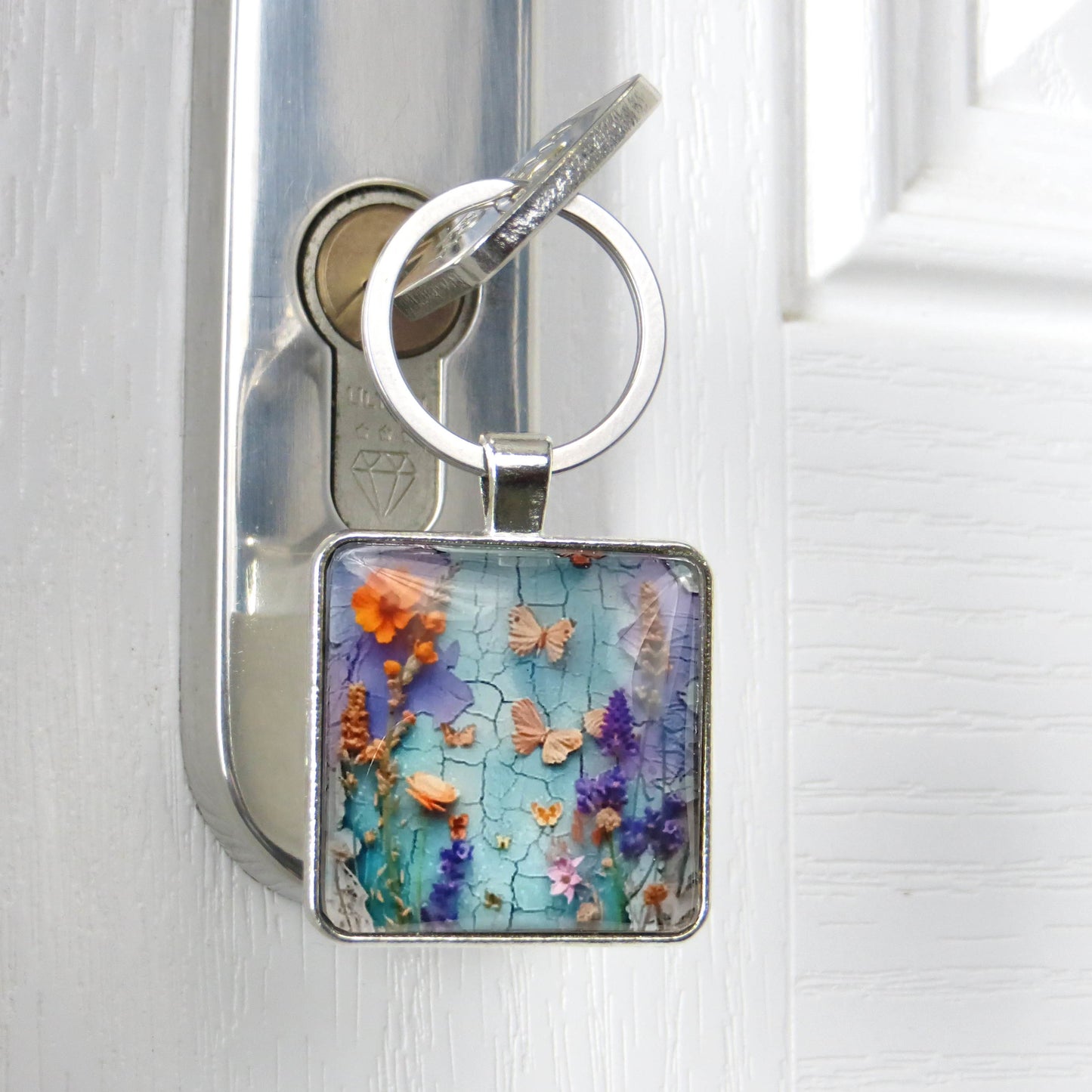 Close up of a square glass cabochon keyring with colourful floral collage design in a metal setting with steel keyring