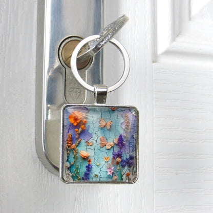 Close up of a square glass cabochon keyring with colourful floral collage design in a metal setting with steel keyring