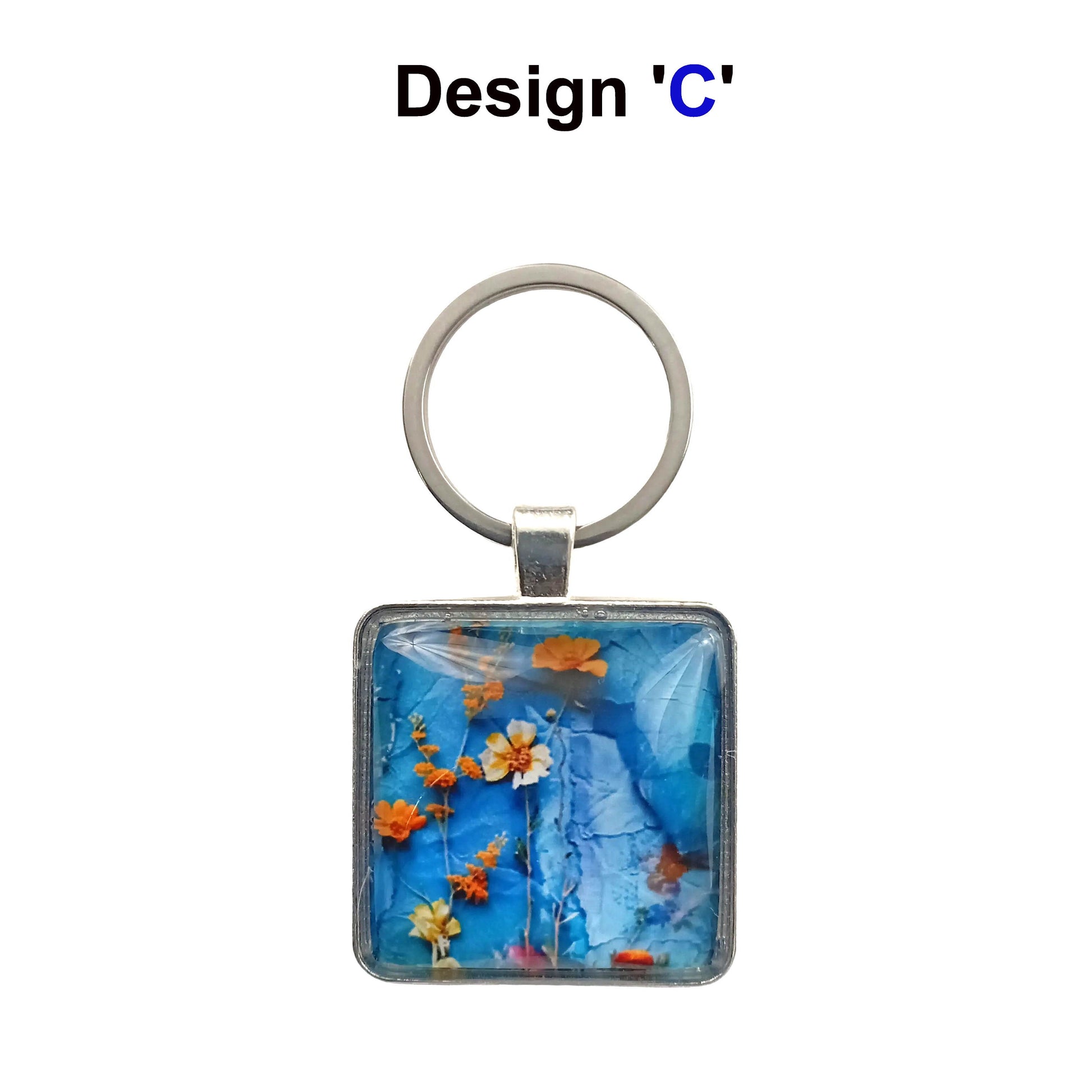 A square glass cabochon keyring with colourful blue and orange floral collage design in a metal frame with steel ring