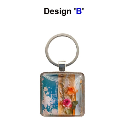 A square glass cabochon keyring with colourful blue and yellow floral collage design in a metal frame with steel ring
