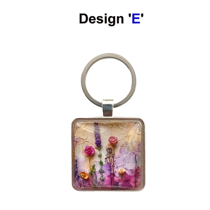 A square glass cabochon keyring with colourful pink and purple floral collage design in a metal frame with steel ring