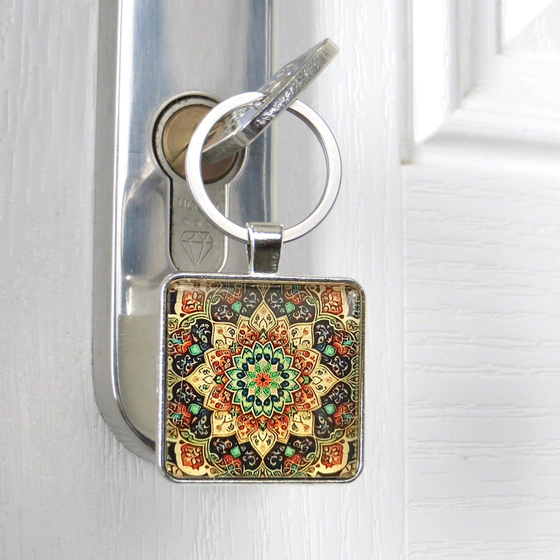 Close up of a square glass cabochon keyring with a colourful mandala pattern