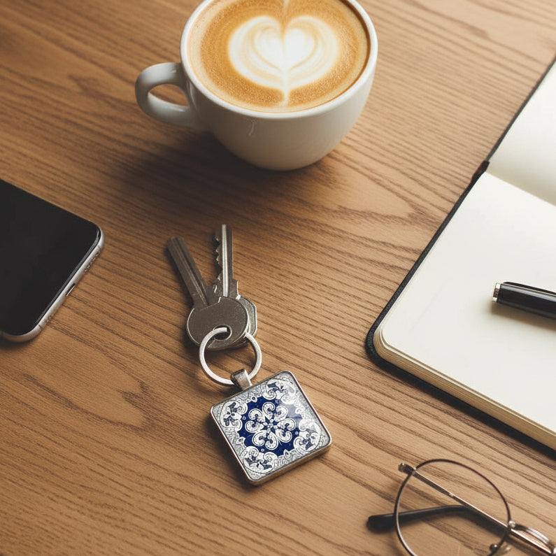 A square cabochon keyring with colourful tile design, laying on a cafe table with accessories