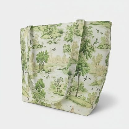 A handmade large cotton tote bag featuring a classic toile-style landscape print with green trees, birds, and a river scene on an off-white background, set against a neutral light grey backdrop.