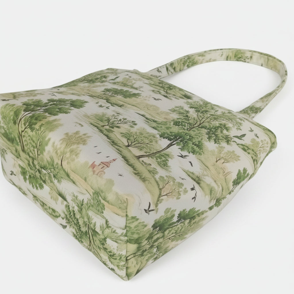 The bottom view of a handmade large cotton tote bag with a green and beige toile-style landscape print on a white background, featuring dual top handles.