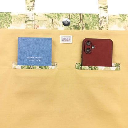 Close up view of a cotton tote bag interior with a notebook and a mobile phone inside two double welt pockets