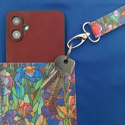 A close-up of a metal key clip with a stained-glass floral pattern strap, a slip pocket with a red smartphone inside a handmade large cotton tote bag with blue interior.