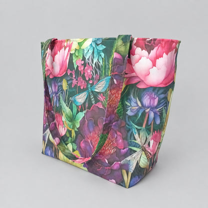 A large handmade cotton tote bag featuring a vibrant, dense botanical and insect pattern with pink flowers, green leaves, and blue dragonflies.