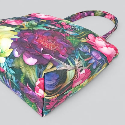The bottom view of a large handmade cotton tote bag with a vibrant, multicoloured floral pattern, featuring pink flowers, green leaves, and a dragonfly design.