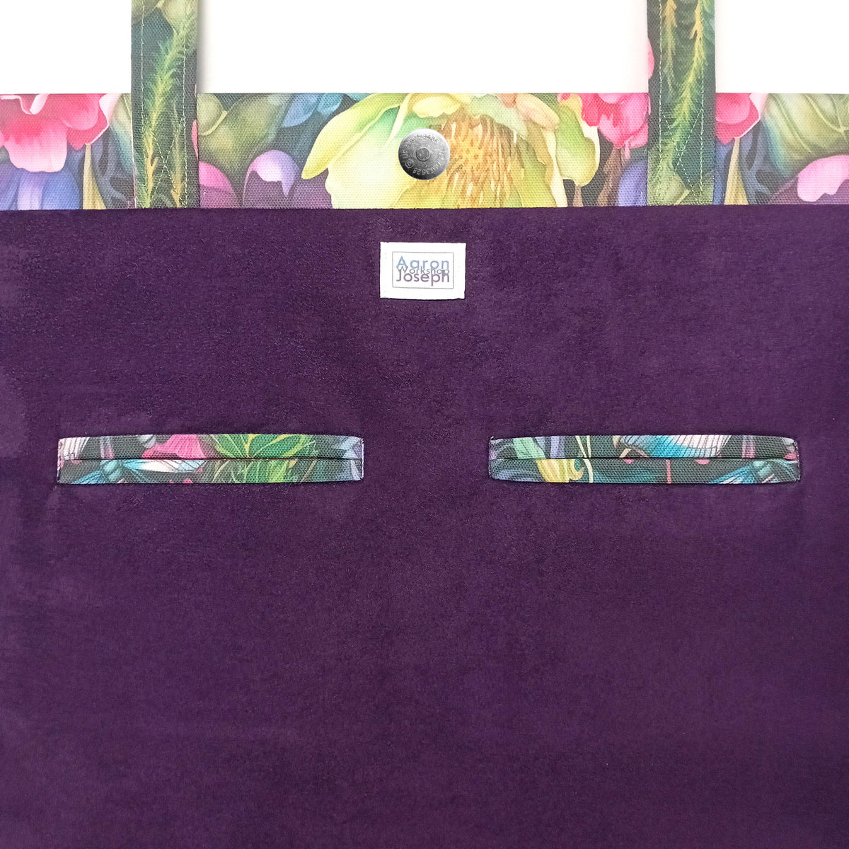 A close-up of a handmade cotton tote bag interior with a purple velvet fabric and a colourful floral and botanical print trim along the top edge and two matching horizontal welt pockets.