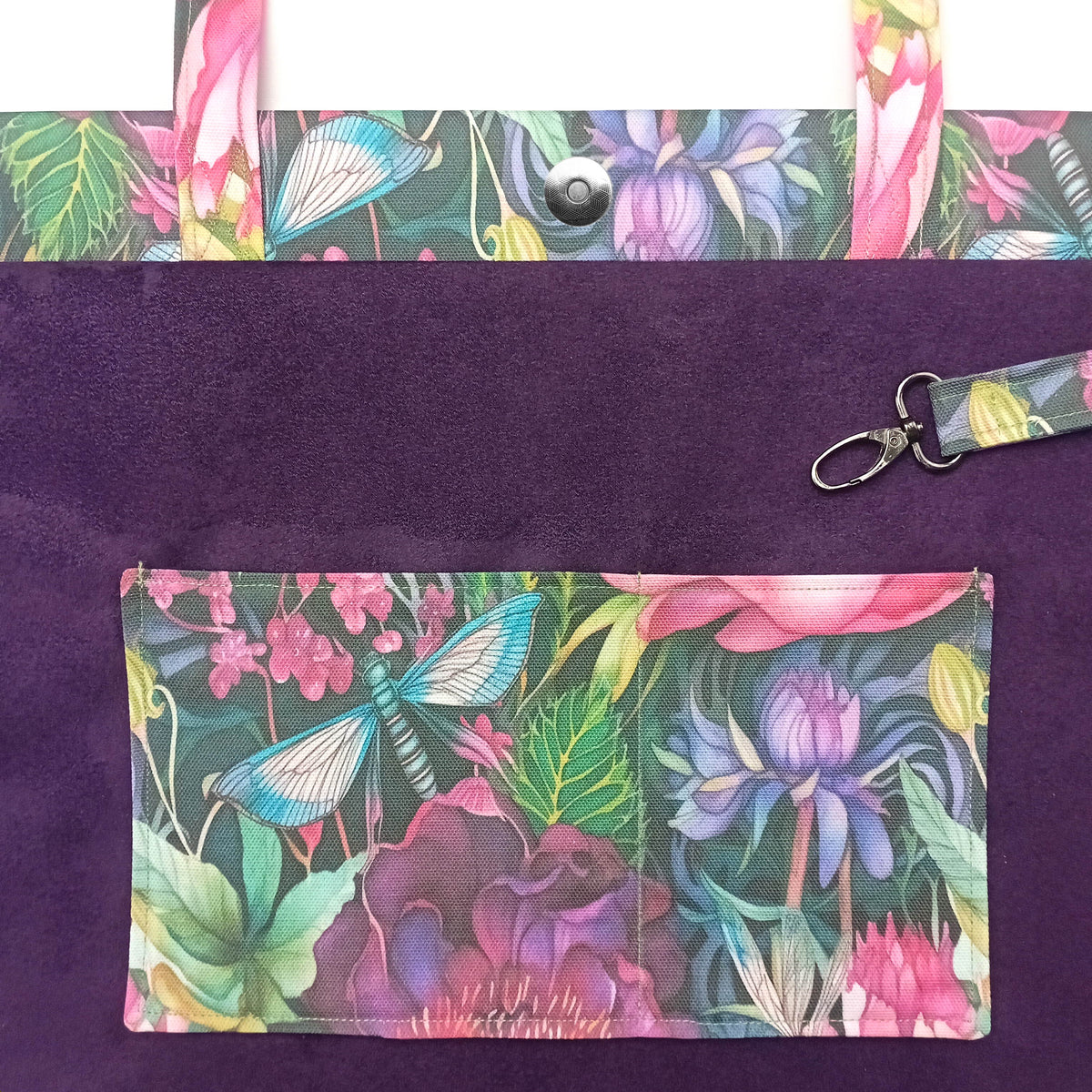 A close-up of a handmade cotton tote bag interior with purple velvet fabric and a colourful floral and butterfly print on the handles, double slip pocket, and attached key clip.