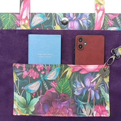 A close-up of a handmade cotton tote bag interior with purple velvet fabric and a colourful floral and butterfly print on the handles, double slip pocket with notebook and mobile phone, and attached key clip.