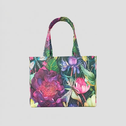 The reverse side of a handmade mini cotton tote bag featuring a vibrant, multicoloured botanical print with large purple and pink flowers, green leaves, and dragonflies, and two top handles.