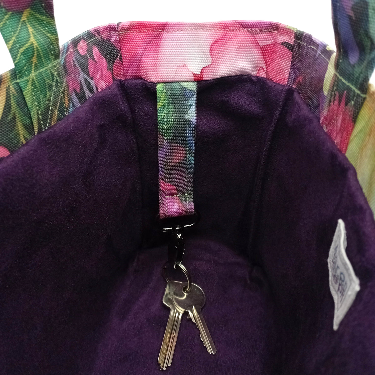 Close-up of a handmade mini cotton tote bag's interior, featuring a deep purple velvet-like lining, a floral-patterned fabric strap with a metal key clip holding two keys, and a floral trim.