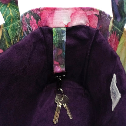 Close-up of a handmade mini cotton tote bag's interior, featuring a deep purple velvet-like lining, a floral-patterned fabric strap with a metal key clip holding two keys, and a floral trim.