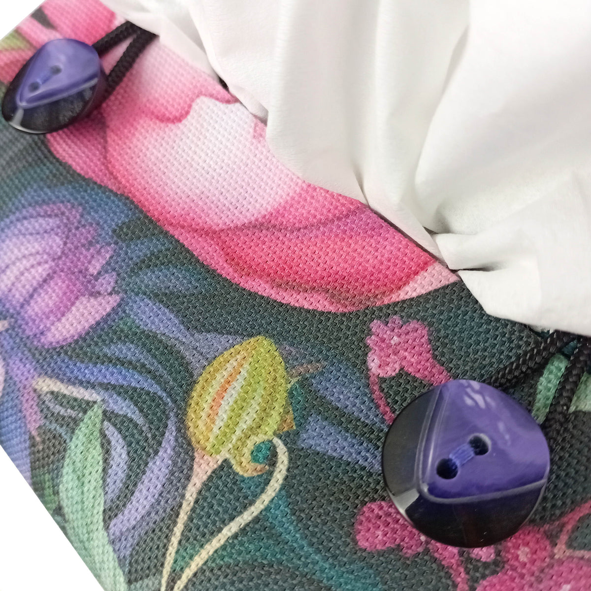 A close-up of a handmade square cotton tissue box cover with a colourful floral and dragonfly print in pink, purple, green, and yellow, featuring a white drawstring and two round purple buttons.