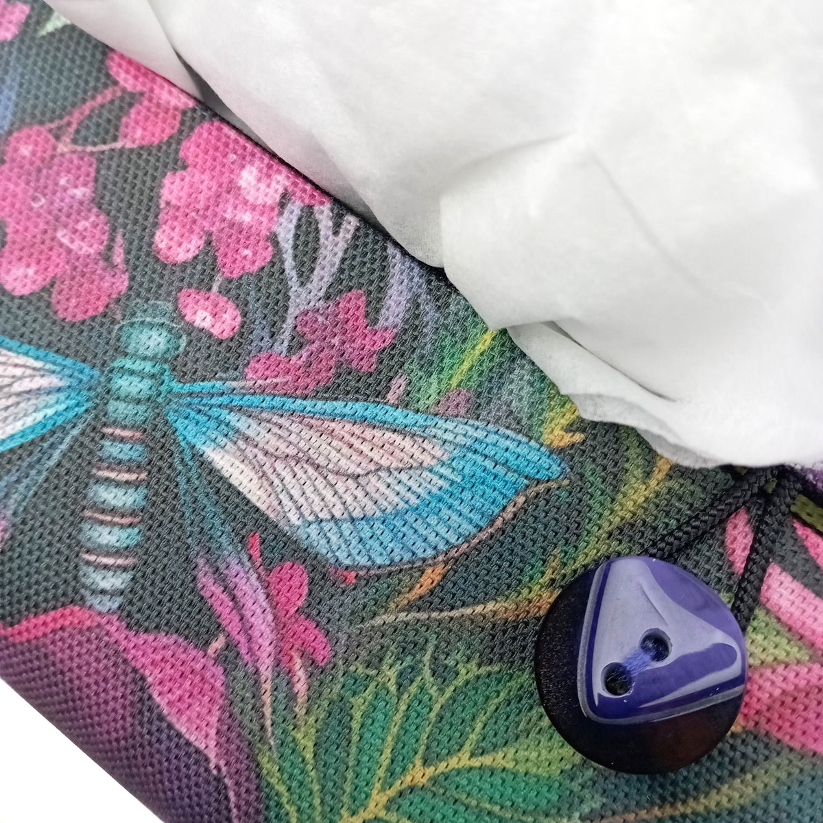 A close up of the button closure on a handmade rectangular cotton tissue box cover with a colourful floral and dragonfly pattern.
