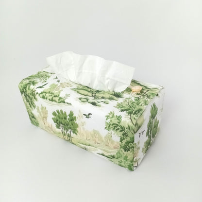The reverse view of a handmade rectangular cotton tissue box cover with a green and white toile-style landscape print on an off-white background.