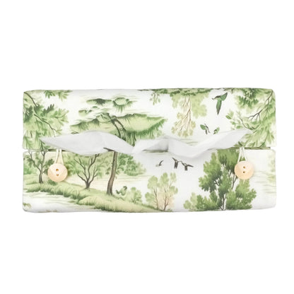Top view of a handmade rectangular cotton tissue box cover with a green and white toile-style landscape print on an off-white background.