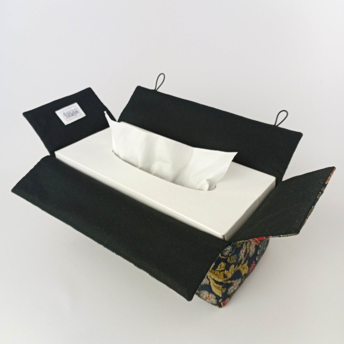 Interior view of a rectangular tissue box cover with a black lining and blue tapestry fabric exterior.