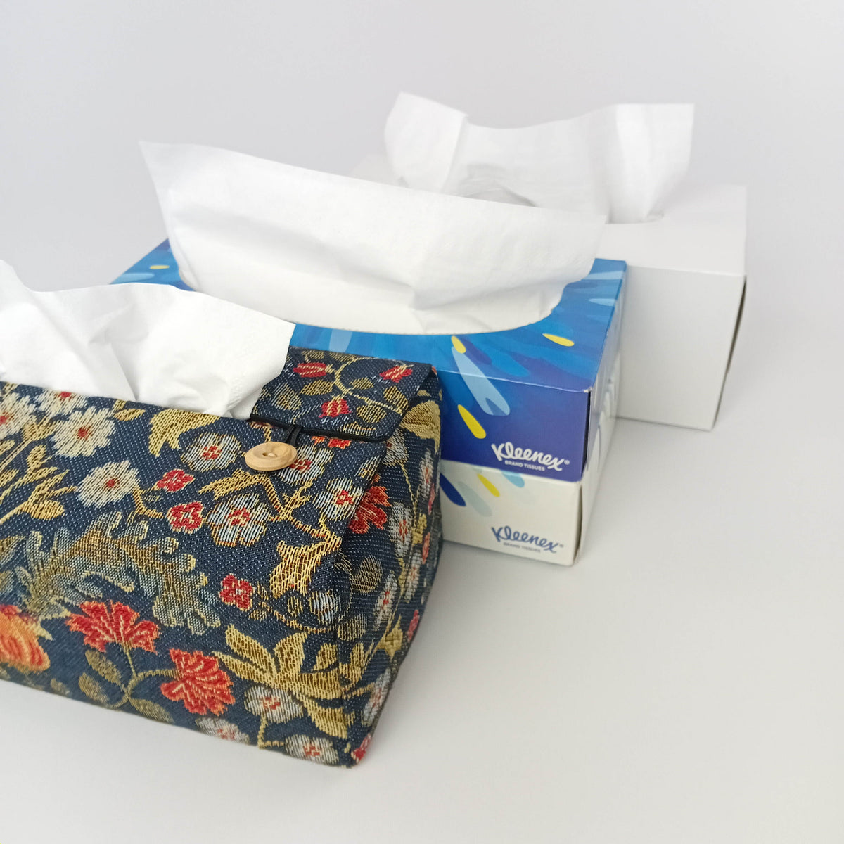 A rectangular tapestry fabric tissue box cover with a navy blue background and a colourful floral pattern, shown with tissue box size options.