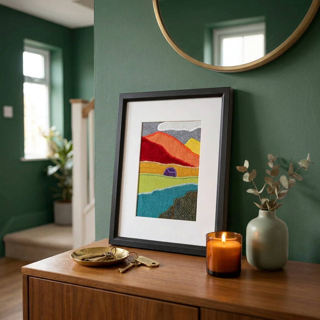 A vertical framed handmade abstract fabric landscape artwork sitting on a console table in a home hallway.