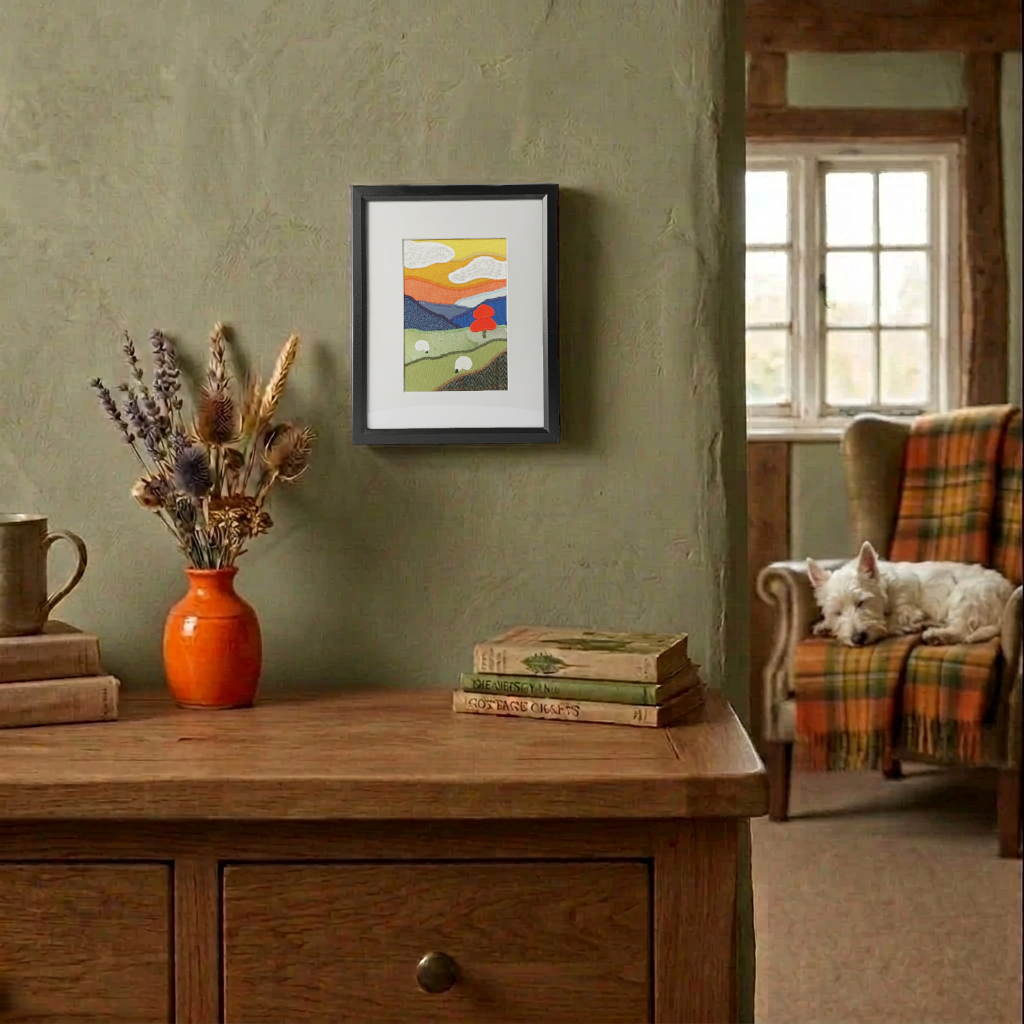 A vertical framed handmade fabric artwork featuring a stylised landscape with rolling green hills, white sheep, and blue mountains hanging on a cottage wall.