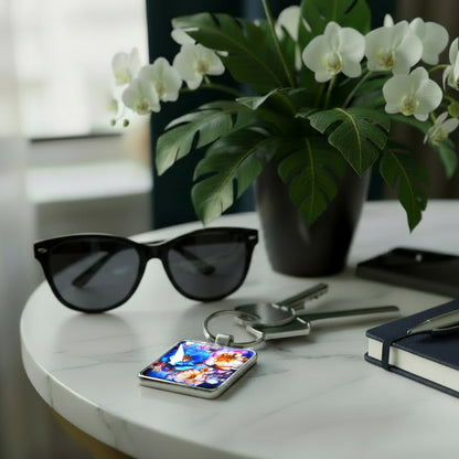 Keychain with a colourful floral design on a table with sunglasses, notebook, pen, and mobile phone.