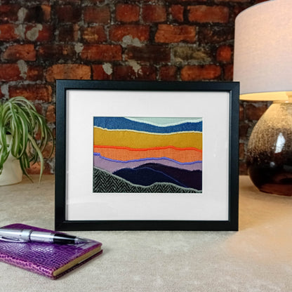 Framed fabric landscape image of a mountaintop and sunset